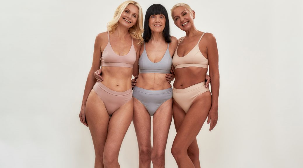 Love yourself. Full length shot of three happy attractive middle aged women in underwear holding hands together and smiling at camera